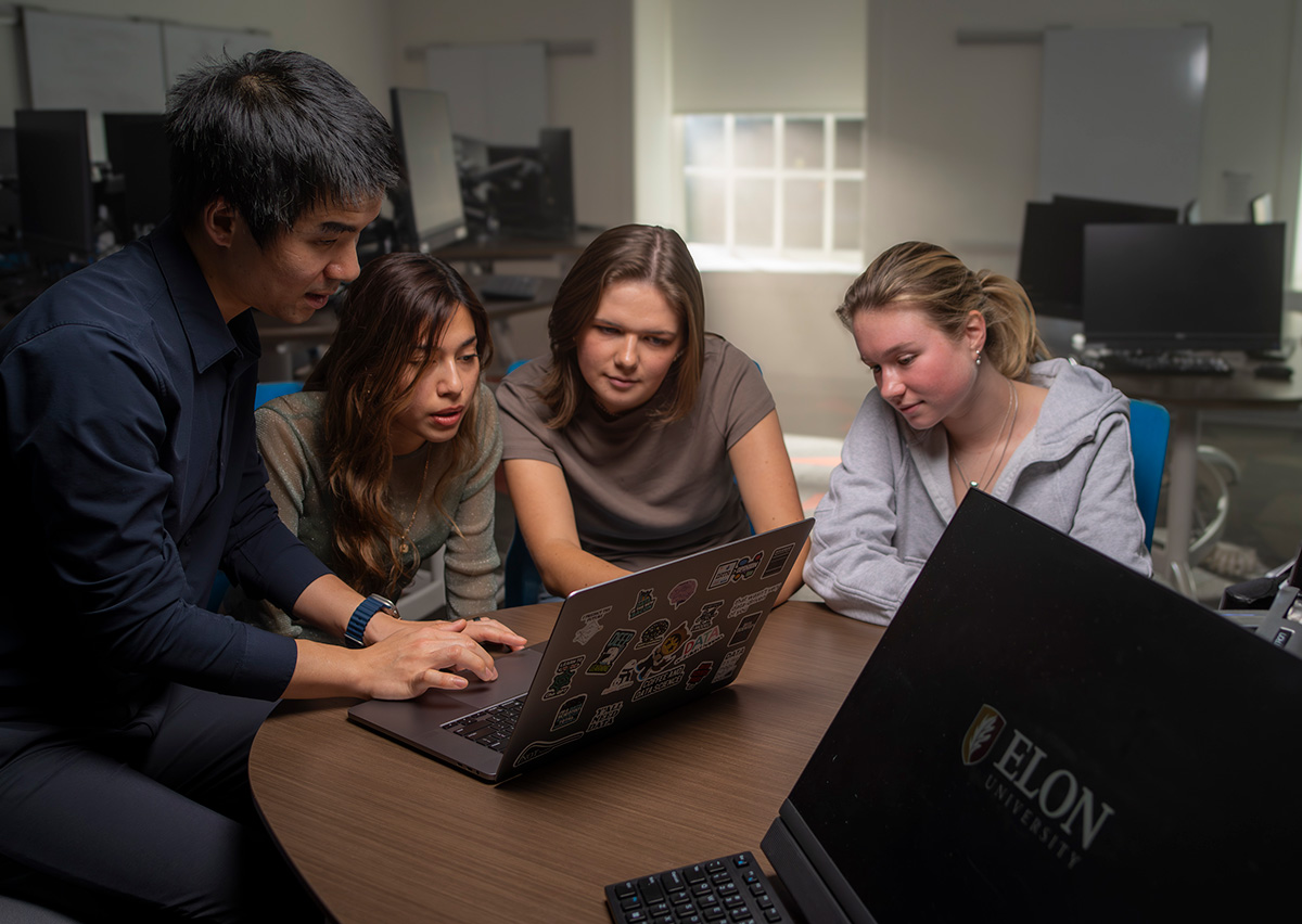 A faculty member works with three MSBA Flex students as they collaborate on a laptop during a hands-on class session in Charlotte.